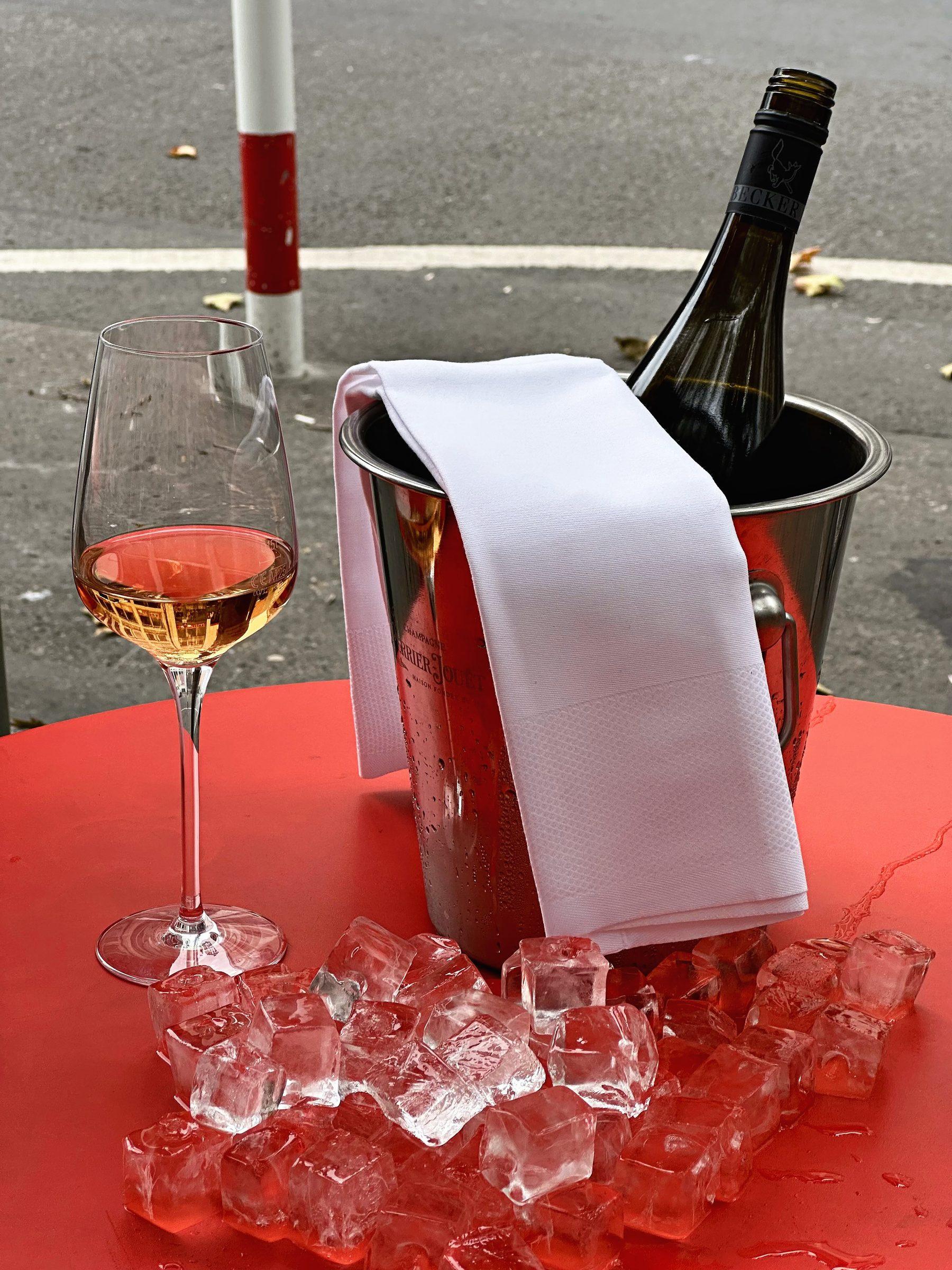 Glas Friedrich Becker Grauburgunder neben einem Eiskübel auf rotem Tisch